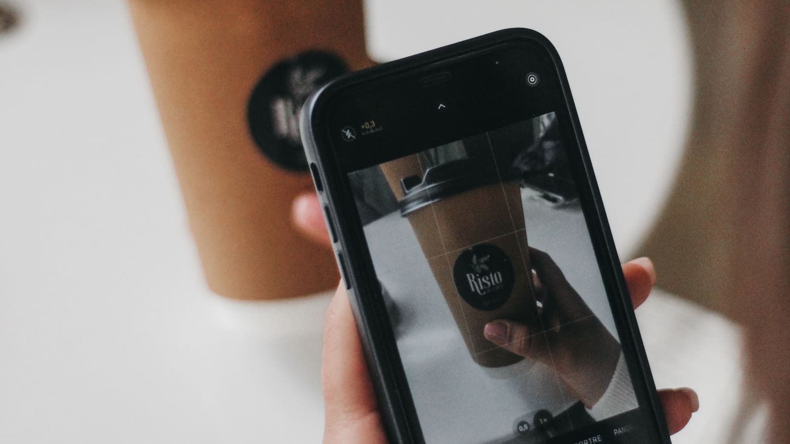 Tangan memotret gelas kopi memakai kamera ponsel