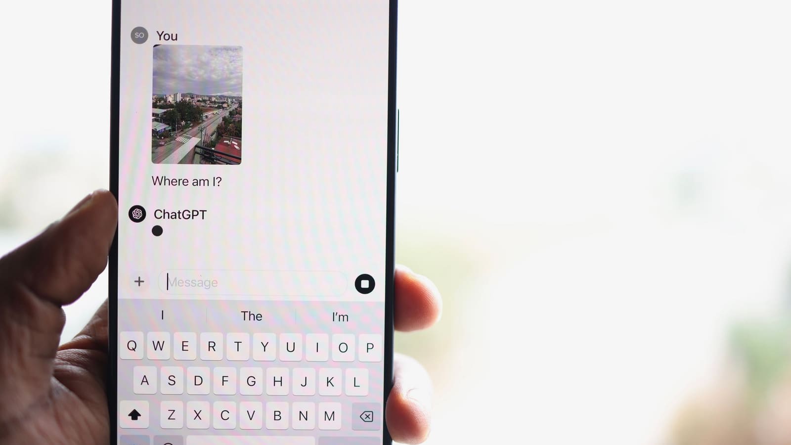 Tangan memegang ponsel dengan percakapan chatbot terbuka dan keyboard menyala