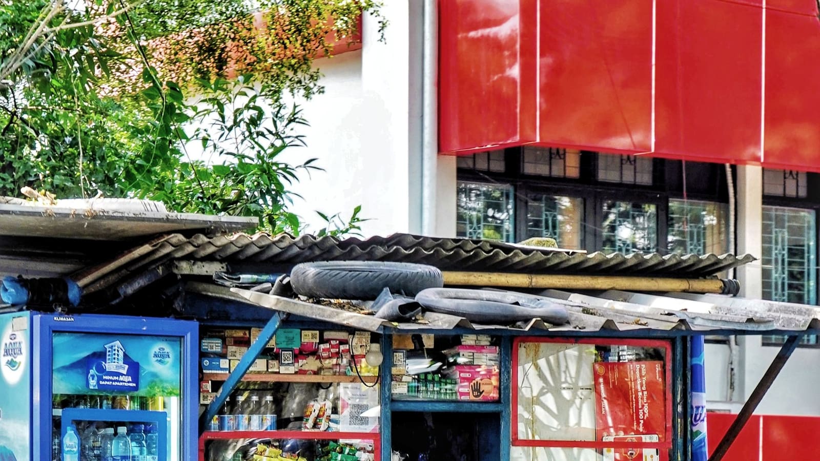 Pemilik warung pinggir jalan duduk di depan kiosnya sambil memegang telepon genggam